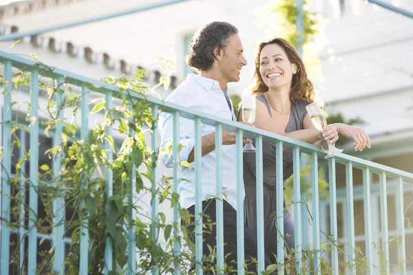 Reifes Paar trinkt Champagner, während es sich im Freien auf den Balkon eines Hotels lehnt. — Stockfoto