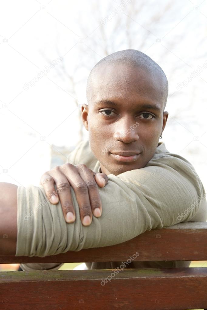 attractive african american man smiling while sitting on a bench in a city park.