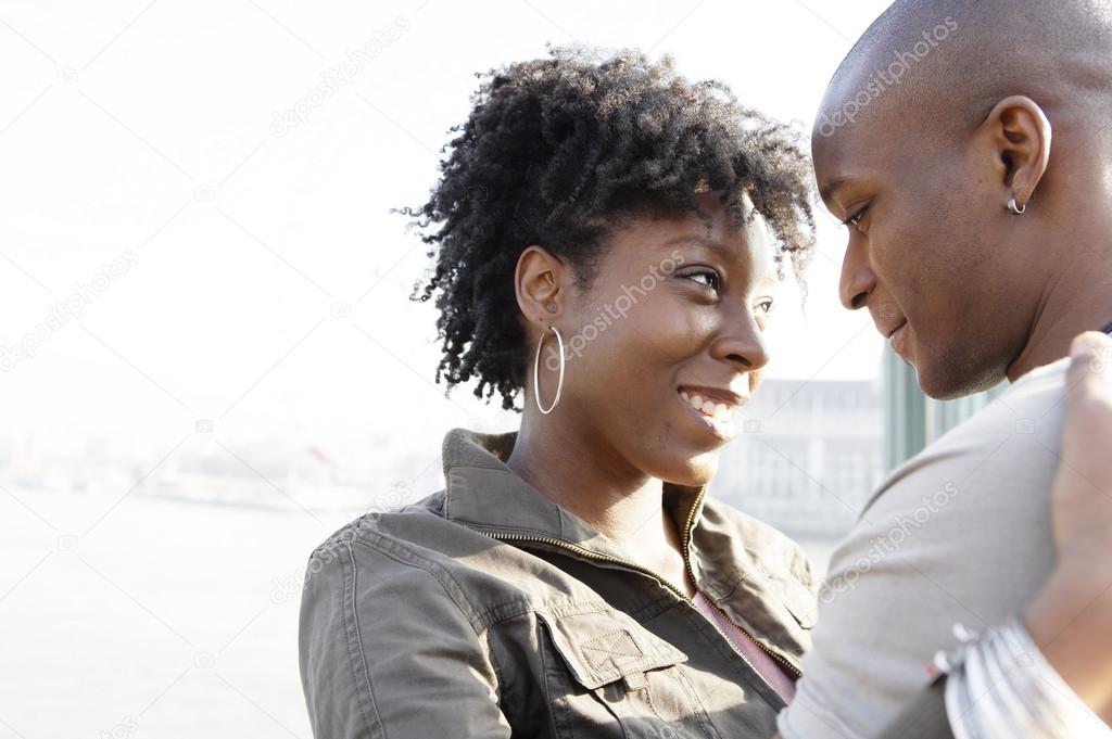 african american couple hugging and smiling by the river Thames in London city, UK.