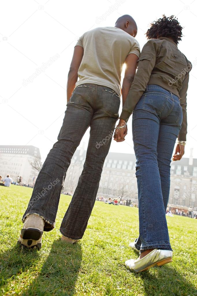 Rear view of figures of a man and woman holding hands while walking through London city on a sunny day.