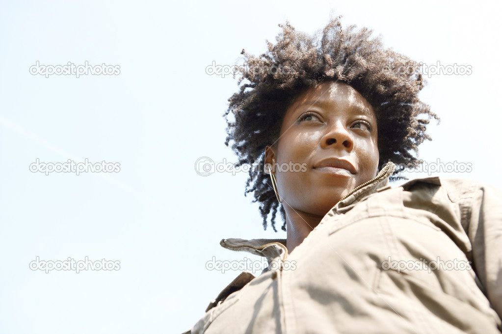 Close up portrait of an attractive young black woman against a blue sky, smiling.