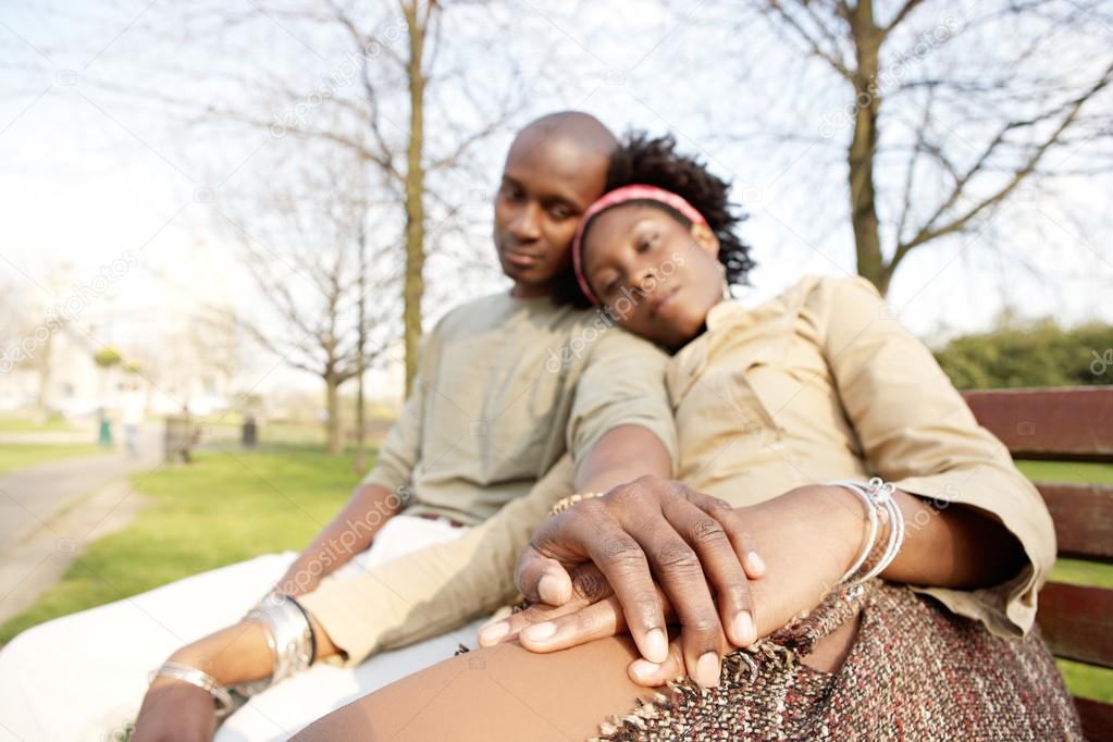 Young attractive black couple sitting down on a bench in the park