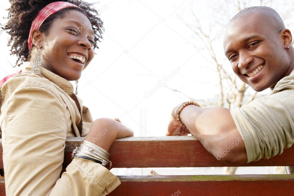 american couple sitting on a wooden bench against the sky