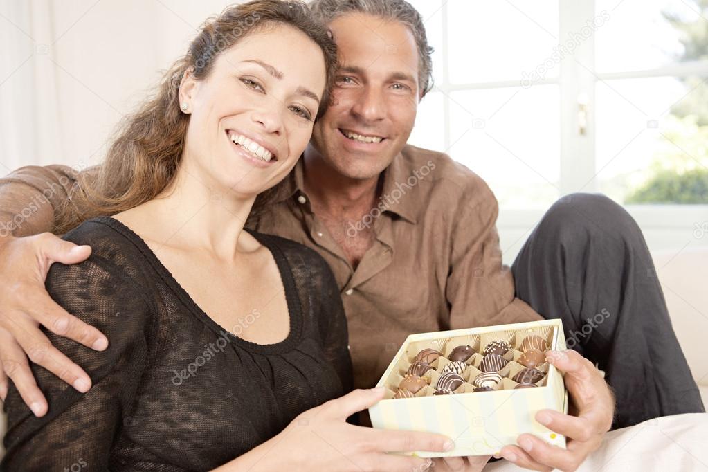Mature couple with box of chocolates at home.