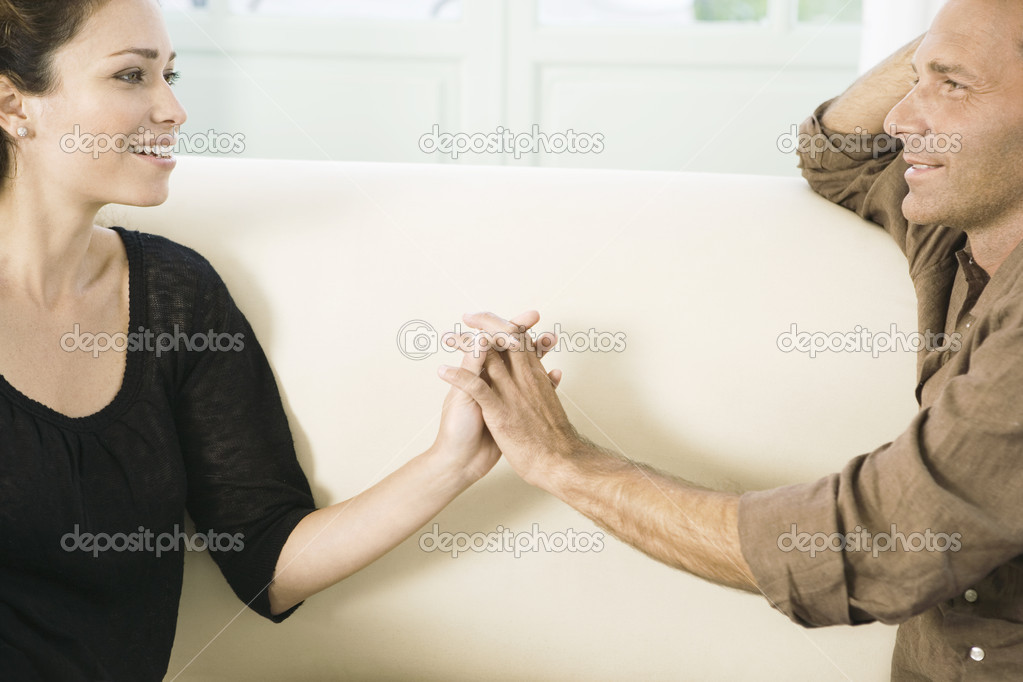 Mature couple touching hands while sitting on a white sofa at home.