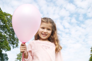 güneşli bir günde parkta bir pembe balon tutan genç gülümseyen kız portresi.