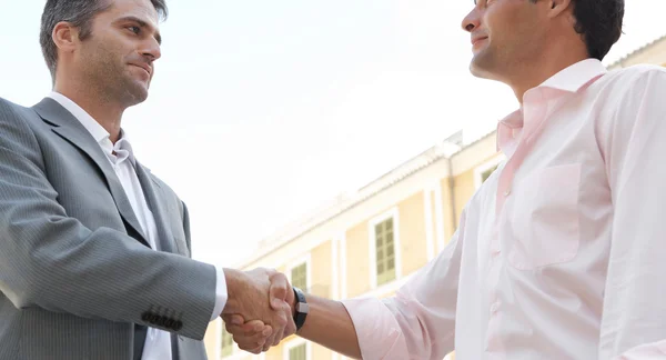 Businessmen shaking hands while standing in front of a classic European building — Stock Photo, Image