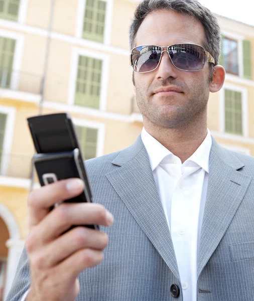 Uomo d'affari che utilizza il suo smartphone mentre si trova di fronte a un classico edificio per uffici in città . — Foto Stock
