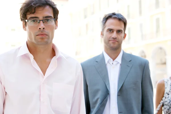 Team van drie werkdagen lopen samen door middel van een klassieke stadsplein met kantoorgebouwen op de achtergrond tijdens een zonnige dag. — Stockfoto