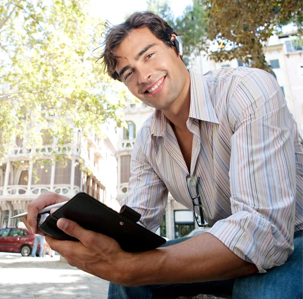 Giovane uomo d'affari casuale utilizzando un dispositivo orecchio mani libere per avere una conversazione — Foto Stock