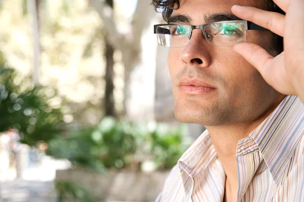 Joven y atractivo hombre de negocios mirando hacia arriba mientras sostiene sus gafas de lectura con la mano . —  Fotos de Stock