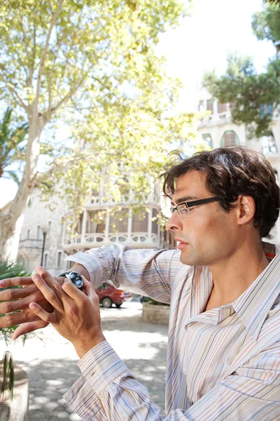 Jeune homme d'affaires vérifiant sa montre tout en se tenant dans un extérieur de ville classique . — Photo