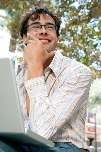 Joven hombre de negocios usando una computadora portátil mientras está sentado en un banco en un parque de la ciudad — Foto de Stock