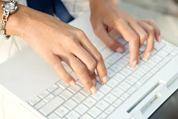Vista detallada de las manos de una joven empresaria escribiendo en una computadora portátil mientras está sentada al aire libre en una ciudad . — Foto de Stock