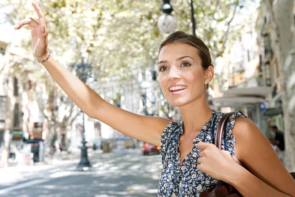 Aantrekkelijke jonge zakenvrouw verhogen haar arm, bel een taxi in een drukke stad, buitenshuis. — Stockfoto