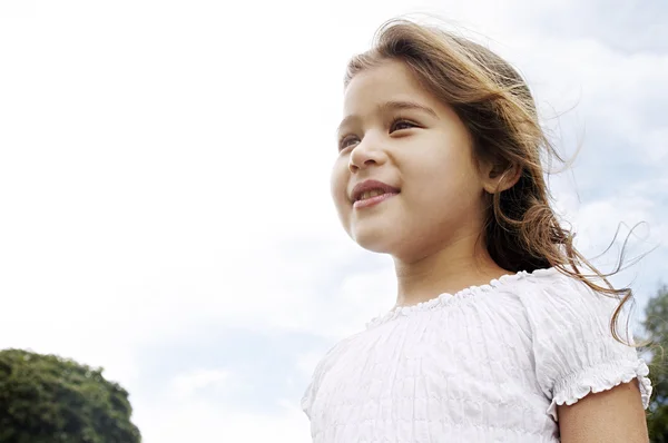 Aspirationele portret van een jong meisje glimlachend in het park met haar waait in de wind. — Stockfoto