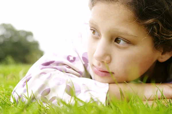 Portrait of a young girl laying down on green grass in the park — Stock Photo, Image