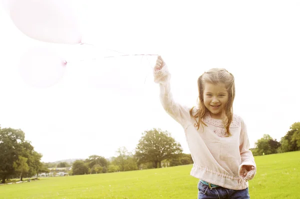 Young girl holding pink balloons in the air and smiling in the park. — Stock Photo, Image