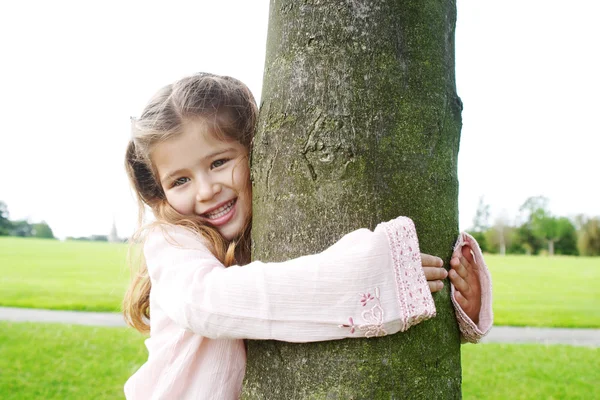 Χαμογελώντας νεαρό κορίτσι αγκαλιάζει ένα δέντρο στο πάρκο. — Φωτογραφία Αρχείου