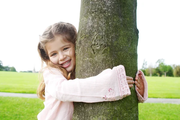 Leende ung flicka krama ett träd i parken. — Stockfoto