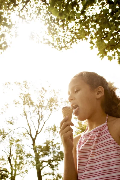 Ritratto di una giovane ragazza che mangia un gelato nel parco, sotto la luce dorata e gli alberi . — Foto Stock