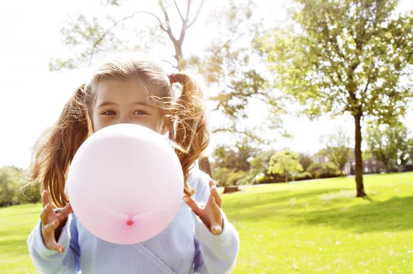 Mladá dívka foukání růžový balón v parku za slunečného dne. — Stock fotografie