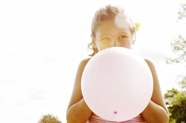 Porträtt av en ung flicka som blåser upp en rosa ballong framför hennes ansikte. — Stockfoto