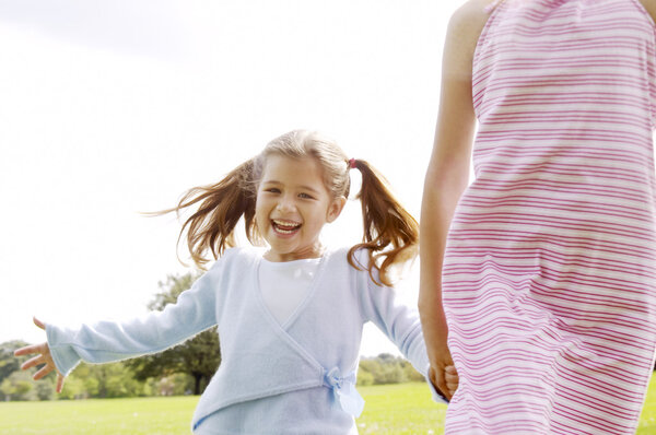 Two girls walking towards the camera in the park, smiling.