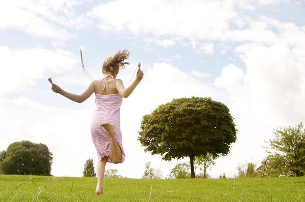 Back view of a young girl skipping in the park with a rope.