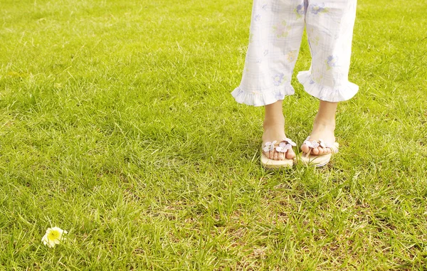 Young girl's feet wearing summer sandals and standing on bright green grass in the park. — Stock Photo, Image