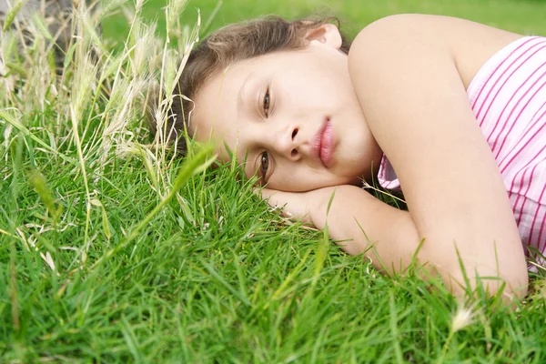 Portrait of a young girl laying down on long green grass in the park, being thoughtful. — Stock Photo, Image