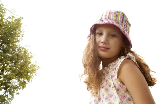 Retrato de uma menina sorrindo para a câmera e vestindo um chapéu listrado colorido no parque . — Fotografia de Stock