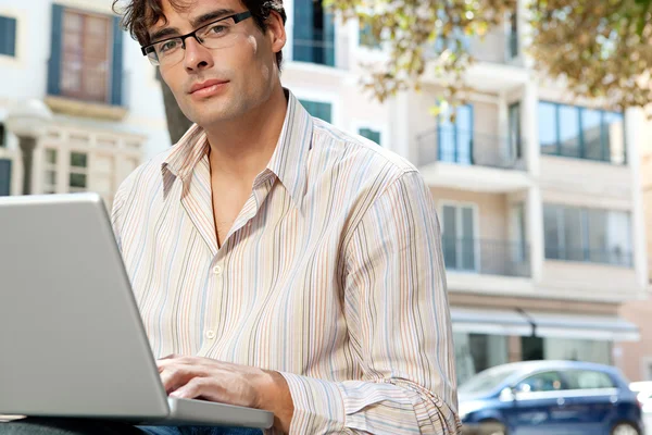 Attraktiver Geschäftsmann mit Brille und Laptop in der Stadt Stockfoto