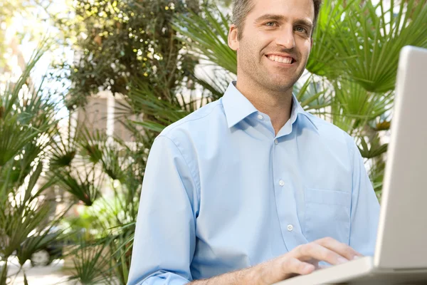 Senior businessman using a laptop computer while sitting on a bench in a city park, outdoors. Stock Photo