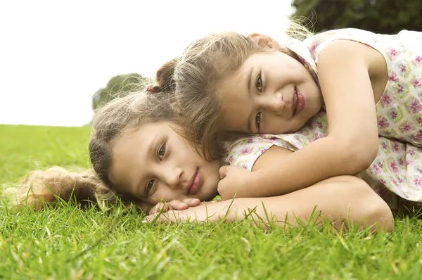 Two sisters laying down on top of each other and smiling in the park. Stock Photo