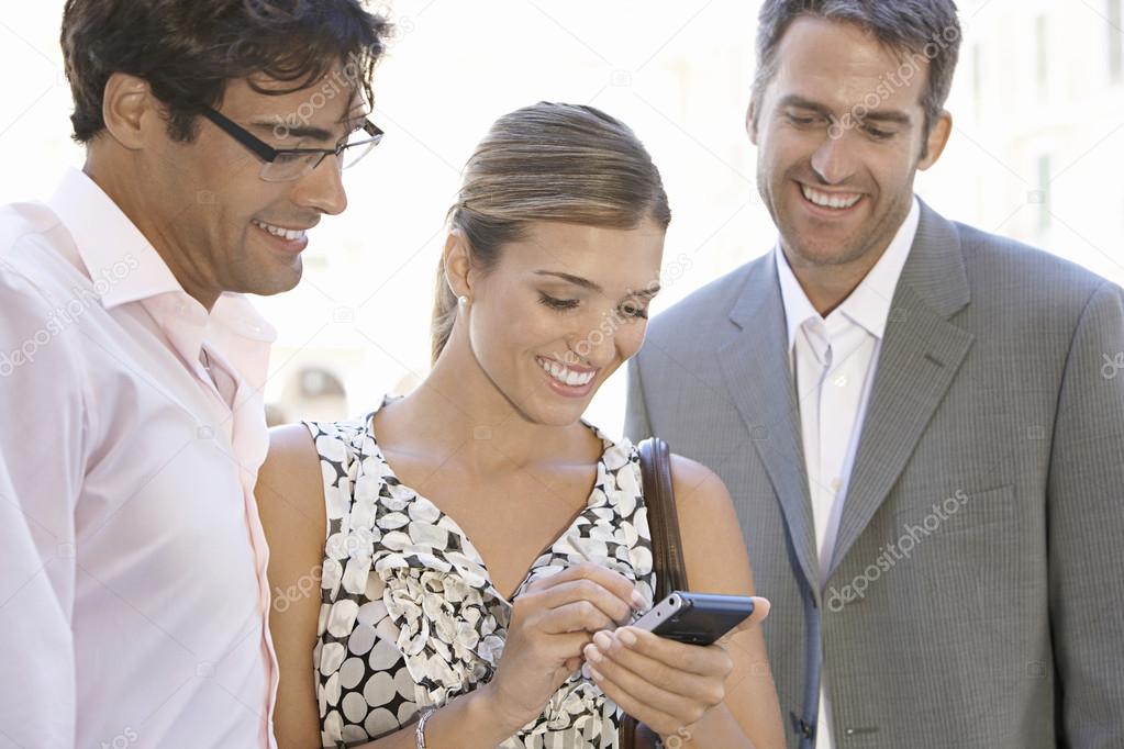 Team of three business having a meeting outdoors and looking at a smartphone.