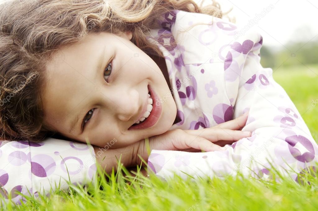 Portrait of a young girl laying down on green grass in the park