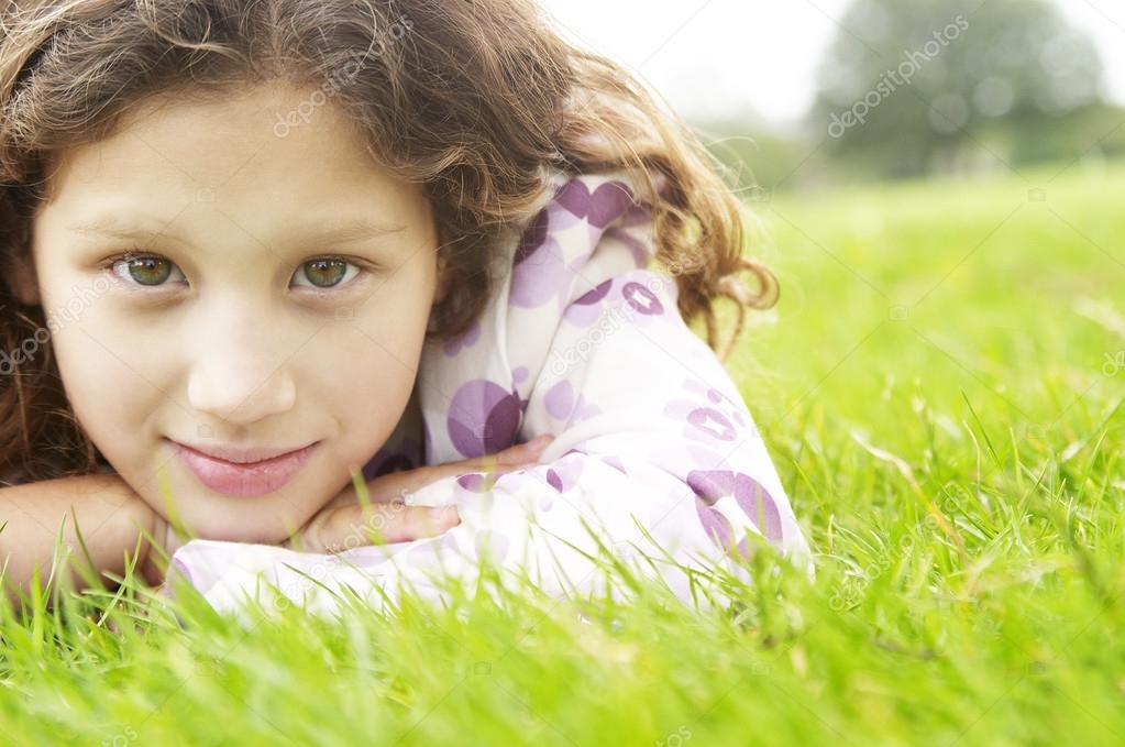 Portrait of a young girl laying down on green grass in the park.
