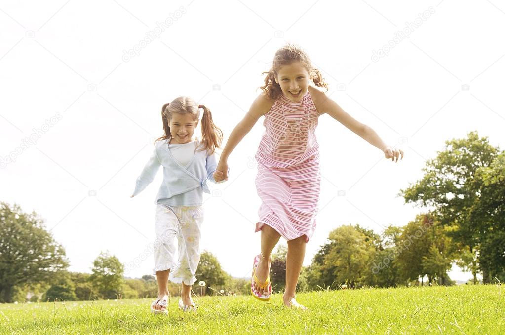 Two girls running towards the camera in the park, smiling.