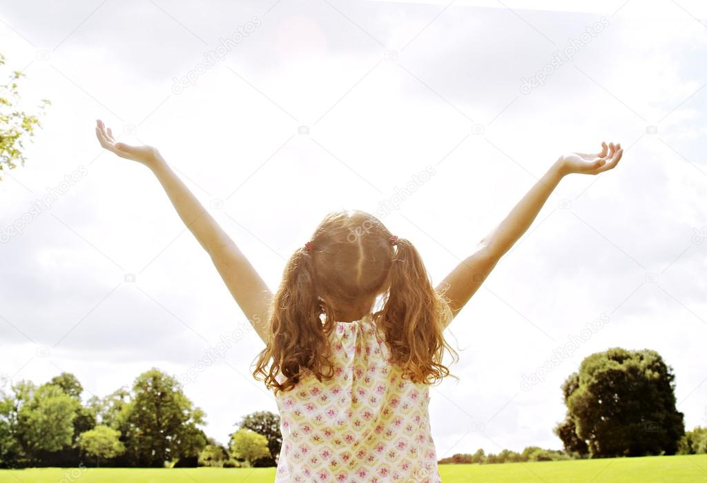 Girl standing in the park with her arms outstretched towards the sky.