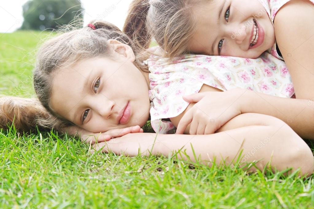 Two young sisters laying down on green grass in the park