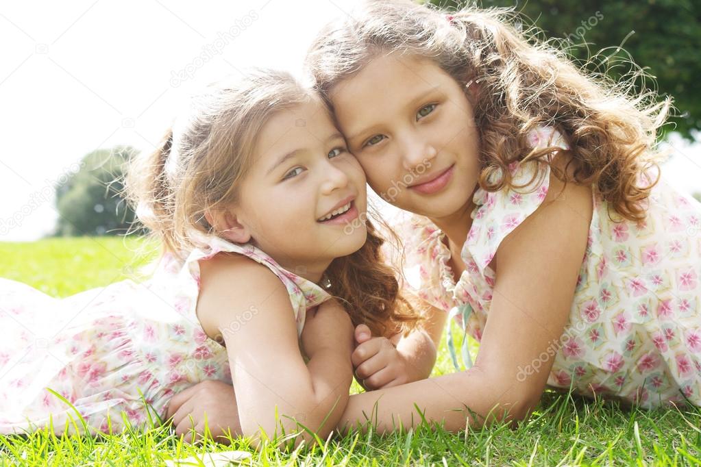 Two sisters laying down on green grass in the park