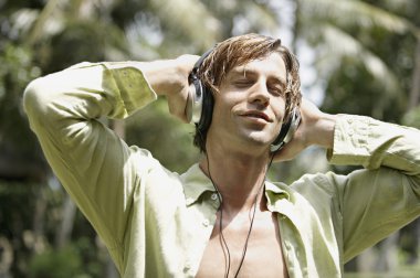 mutlu bir adam bir tropik bahçe kulaklık ile müzik dinlemek.