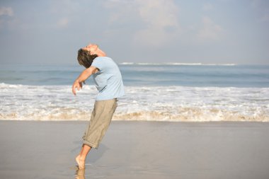Young attractive man dancing on the beach, bending backwards while on tip toes. clipart