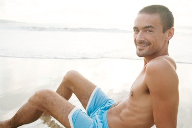 gün batımında altın kum deniz kıyısında oturan genç adam dövmek