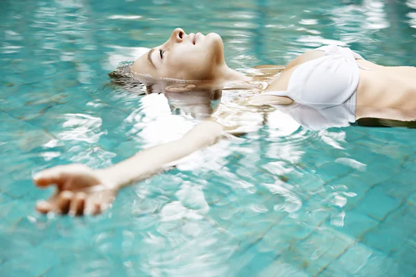 Yüzme havuzunda kolları açık yüzen çekici genç bir kadın..