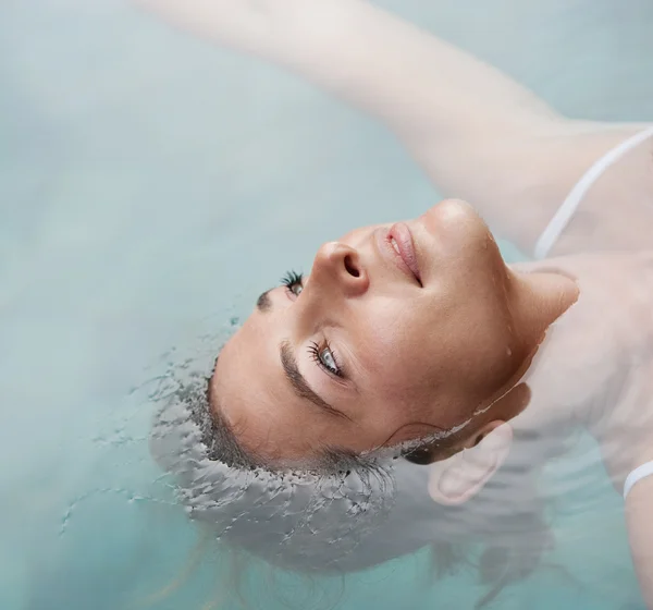 Vista de cerca de una mujer joven flotando en el agua mientras está en una piscina de vacaciones . —  Fotos de Stock