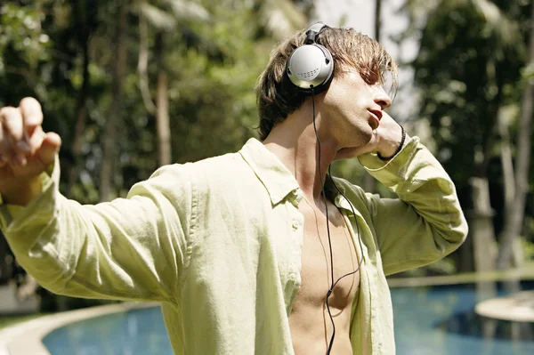 Side view of a young man on vacation, listening to musing with headphones — Stock Photo, Image