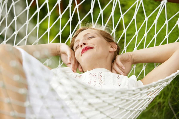 Jovem mulher atraente que coloca e relaxa em uma rede branca em um jardim . — Fotografia de Stock