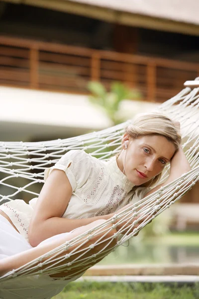 Attractive young woman listening to music while sitting on a hammock — Stock Photo, Image